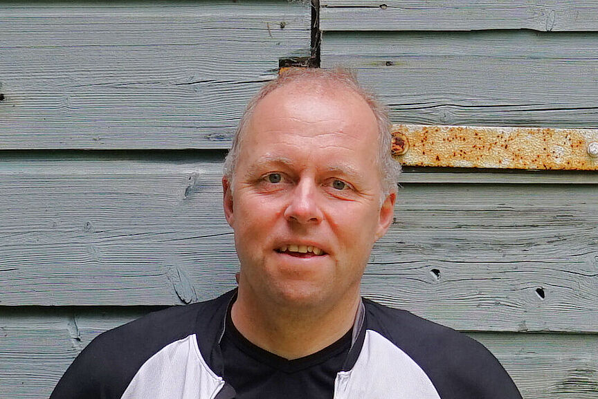 Karsten Karsten Pehlke im Radtrikot vor einer blaugrauen Wand aus Holz